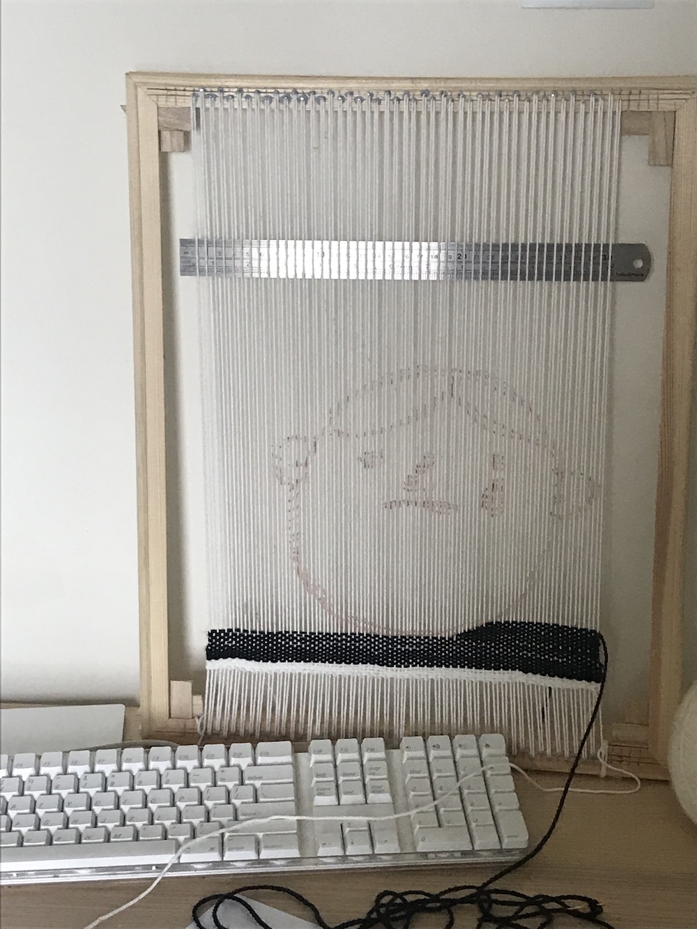 a loom with the weft being filled in in black and a cartoon of a crying face drawn as a guide on the warp
