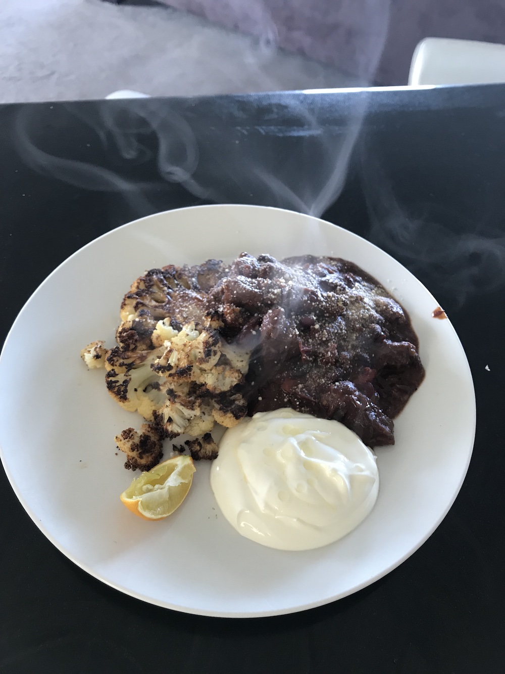 a plate with burnt cauliflower, chilli beef, yoghurt and lemon on it, steaming