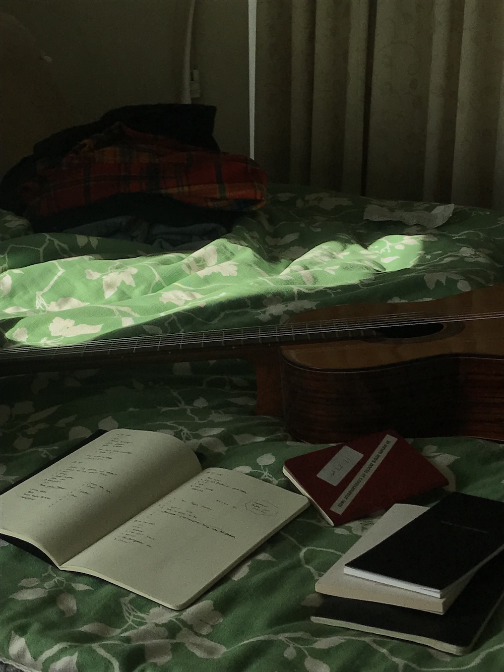 green bedspread with a guitar and some notebooks on it, in the sun