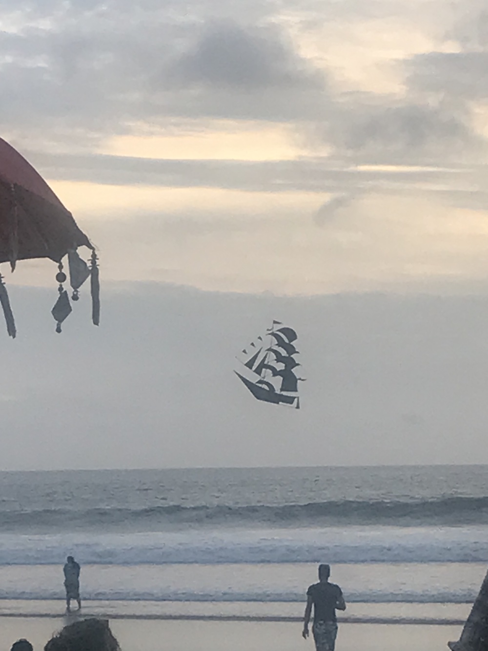 A pirate ship shaped kite flying at a beach