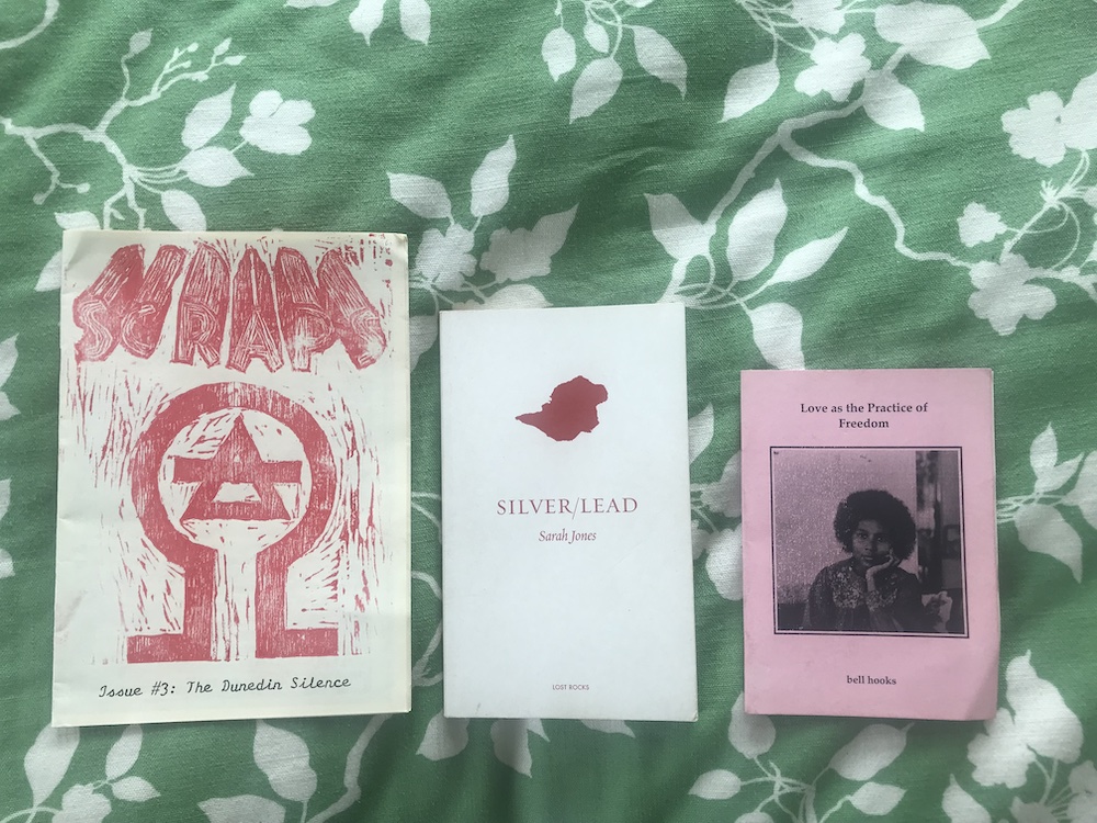 a green bedspread with these three books ontop: Love as the Practice of Freedom by Bell Hooks, Silver/Lead by Sarah Jones, Scraps issue 3 the dunedin silence by Spencer Hall