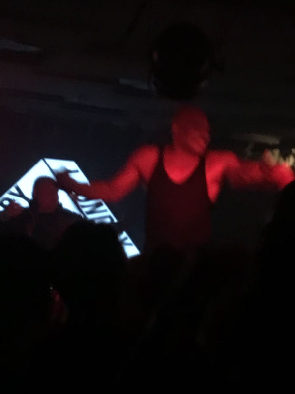 a dark crowded venue, a big man is glowing red and jumping around in a black singlet