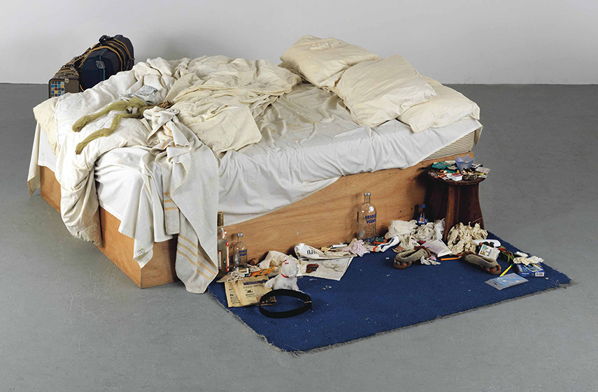 a messy bed with bottles of alcohol and trash on the ground beside it, sitting in a gallery
