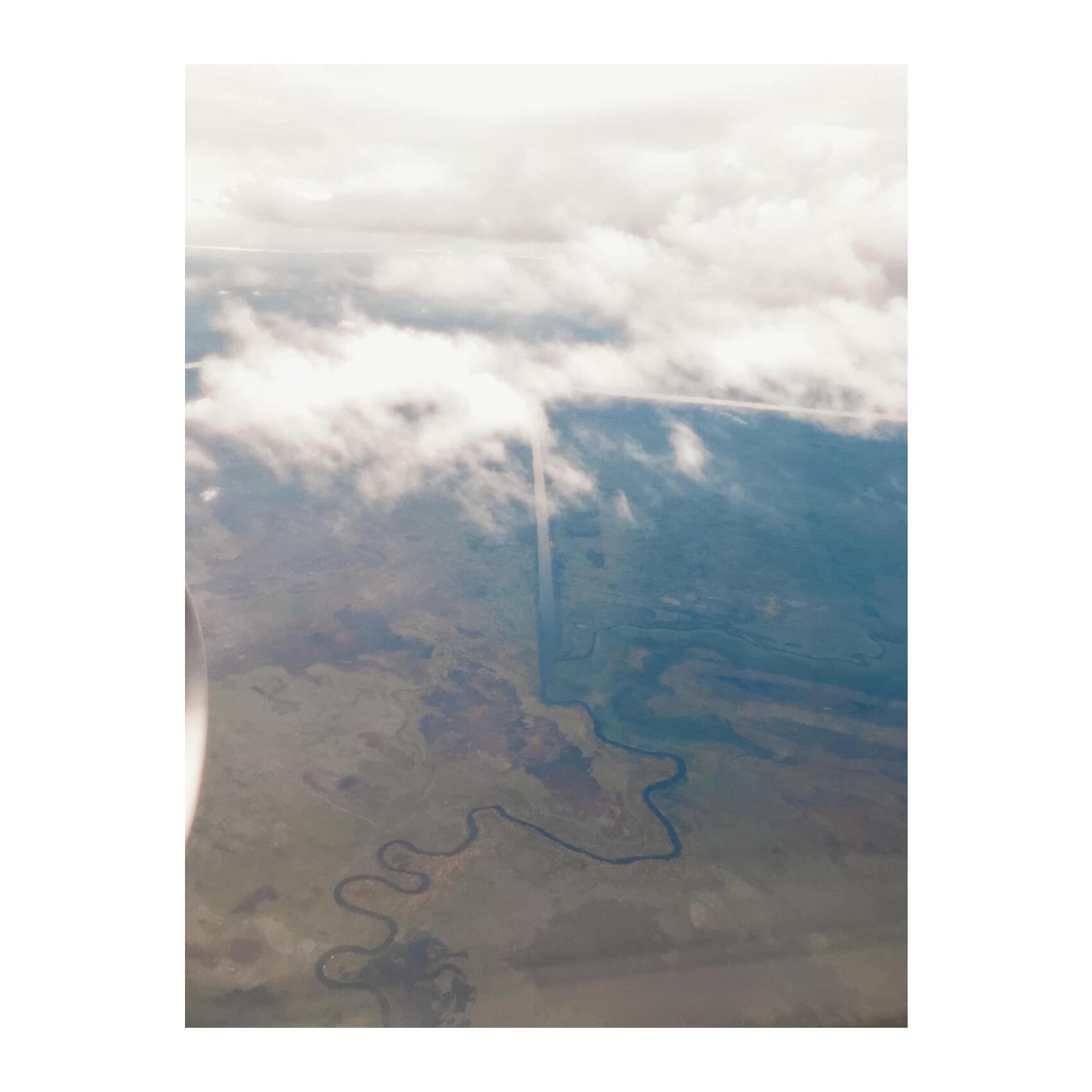 a plane window view of a small river running into a long straight irrigation channel